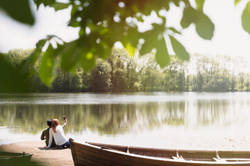 Couple camera phone taking selfie on sunny lakeside dock next to canoe