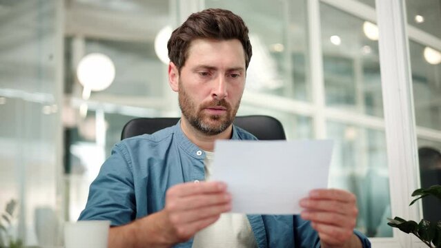Angry stressed businessman opening envelope reading bad terrible news in mail letter. Mad man feels frustrated about high bills, dismissal notice, bank debt, tax invoice, mistake sits at office desk.