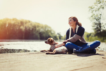 Smiling woman and dog relaxing on sunny lakeside dock