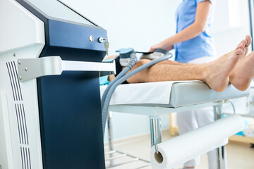 Beautician therapist applying burn fat and build muscles treatment in beauty salon to young man.
