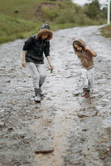 two happy little girls of European appearance playing in puddles during rain in summer. children are playing in the rain. child playing in nature outdoors. the girl enjoys the rain.