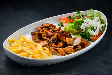 Shawarma chicken meat with french fries and a salad of pickled cucumbers, tomatoes, carrots, lettuce and parsley.