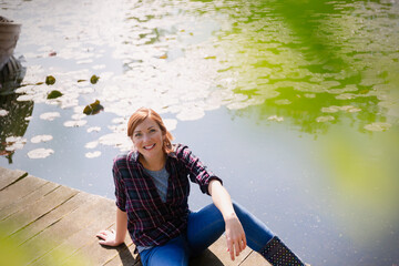 Portrait smiling woman sitting on sunny lakeside dock