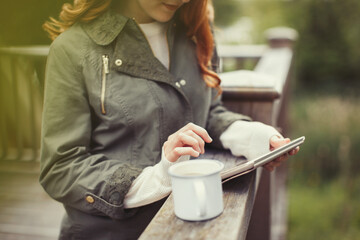 Woman drinking coffee using digital tablet at balcony railing