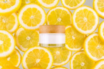 Top view photo of white jar of cream bottle without label in the middle halves and whole yellow lemons on yellow background with blank space.