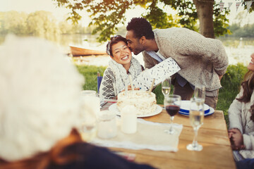 Boyfriend kissing girlfriend birthday gift at lakeside patio table