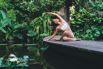 Fototapeta premium Harmony and meditation training during morning yoga at pond, happy Caucasian female yogi in sportswear sitting in flexible pose during hatha practice for exercising body concentration in asana