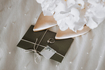 wedding accessories in light colors, shoes, a wedding ring and a wedding bouquet. Invitation from embossed paper in green color