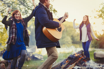 Friends dancing and playing guitar around campfire
