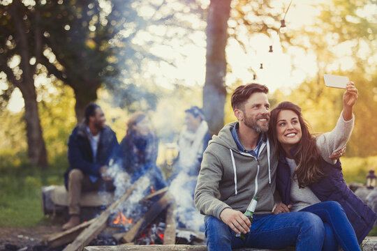 Smiling couple taking selfie with camera phone near campfire