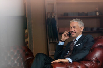 Smiling businessman talking on cell phone in menswear shop