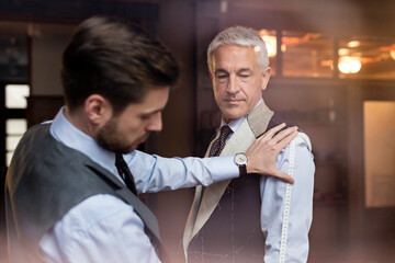Tailor fitting businessman for suit in menswear shop