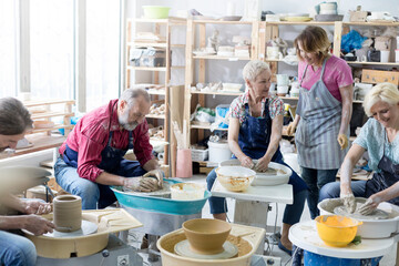 Mature students using pottery wheels in studio - obrazy, fototapety, plakaty