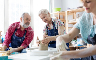 Senior couple using pottery wheel in studio