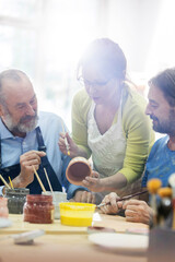 Teacher guiding mature men painting pottery in studio