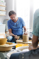 Fototapeta na wymiar Mature man using pottery wheel in studio