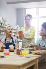 Obraz na płótnie Canvas Teacher guiding mature students painting pottery in studio