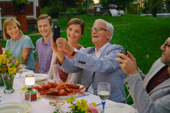 Senior man taking selfie with family at summer garden party dinner