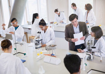 Science professor college students using microscopes in science laboratory classroom