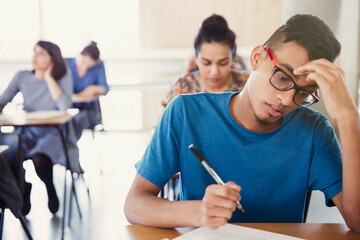 Serious male college student taking test at desk in classroom