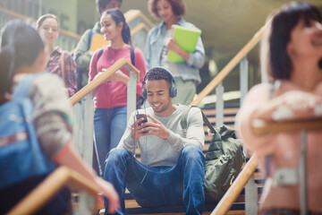 Male college student listening to mp3 player in busy stairway