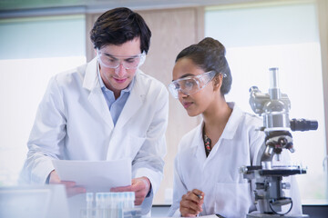 College students conducting scientific experiment at microscope in science laboratory classroom