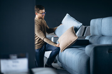 Young man buying pillows and sofa in furniture store