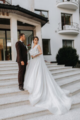 Groom and bride walking outdoors near a posh hotel. A long train of dress on the steps