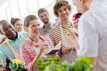 Eager students taking notes listening to chef teacher in cooking class kitchen