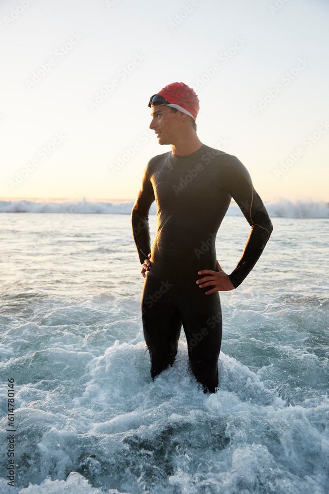 Wall mural male triathlete in wet suit standing in ocean surf