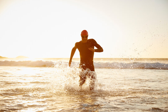 Male triathlete running out of ocean - Powered by Adobe