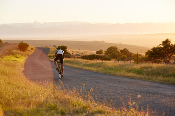 Male triathlete cyclist cycling on sunny rural road at sunrise - obrazy, fototapety, plakaty
