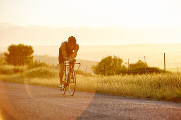 Male triathlete cyclist cycling on sunny rural road at sunrise