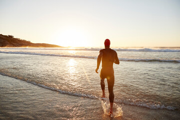 Male triathlete swimmer in wet suit running into ocean surf at sunrise