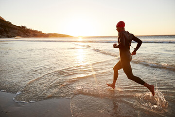 Male triathlete swimmer in wet suit running into ocean surf at sunrise