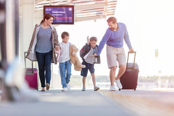 Fototapeta na wymiar Family walking pulling suitcases at train station
