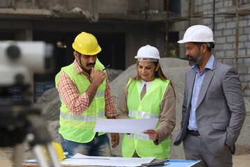Indian construction workers. Construction engineers working on a builder construction site. Wearing white and yellow helmet analyzing blueprint of property. Reporting, maintaining the work in progress