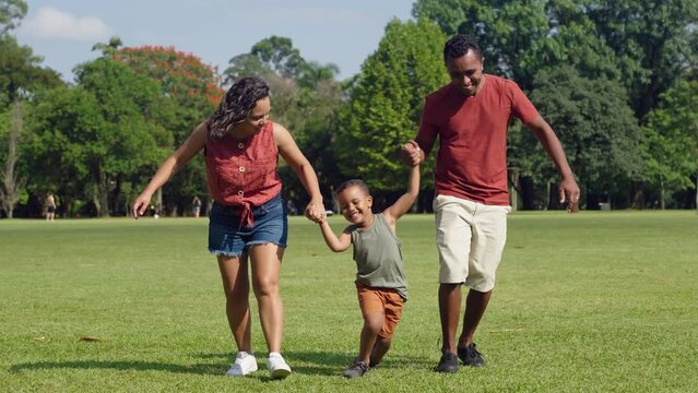 Cute latino boy and his parents are playing in the park. Family have fun during a weekend in nature.
