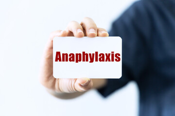 Anaphylaxis text on blank business card being held by a woman's hand with blurred background. Business concept about Anaphylaxis.
