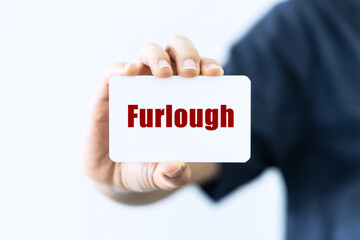 Furlough text on blank business card being held by a woman's hand with blurred background. Business concept about furlough.