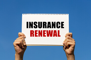 Insurance renewal text on notebook paper held by 2 hands with isolated blue sky background. This message can be used as business concept about insurance renewal.