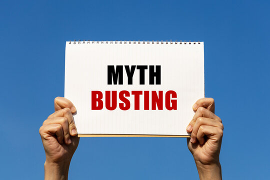 Myth busting text on notebook paper held by 2 hands with isolated blue sky background. This message can be used as business concept about myth busting.