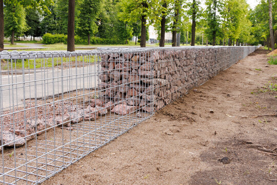 Construction of a gabion wall. The process of filling the basket with granite stones. Selective focus.