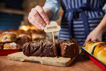 Sales Assistant In Bakery Putting Homemade Label Into Freshly Baked Baked Chocolate Brownies