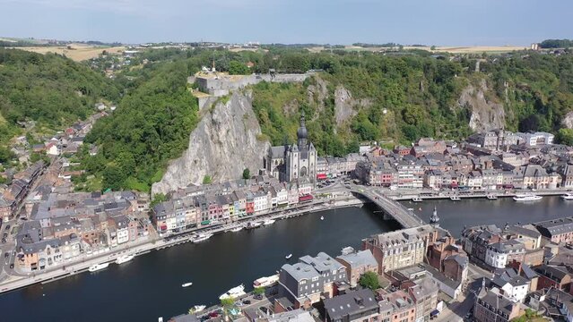 Scenic summer view of Dinant cityscape on banks of river Meuse overlooking Collegiate Church of Notre Dame and fortified Citadel on top of cliff overgrown with green trees, Namur province, Belgium