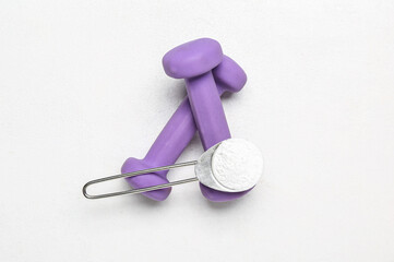 Scoop with amino acid supplement and dumbbells on light background