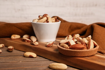 Board with bowl and plate of tasty Brazil nuts on wooden background, closeup