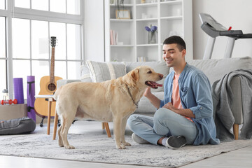Young man with cute Labrador dog sitting on floor at home