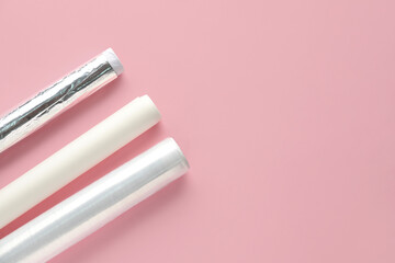 Rolls of aluminium foil, baking paper and food film on pink background