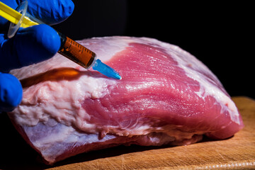 Injection from a syringe into raw meat on a dark background.Conceptual illustration of hormones and...